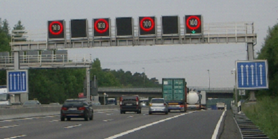 Vier dynamische Anzeigen weisen auf einer dreispurigen Strecke auf Tempolimit 100 und mittels grünem Pfeil unter der Anzeige rechts auf eine TSF hin.