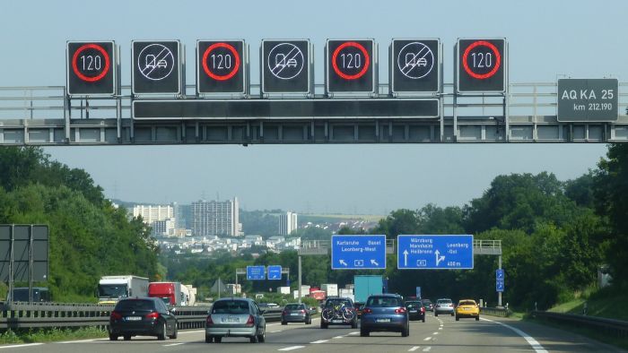Eine Verkehrsbeeinflussungsanlage steuert den Verkehr auf einer vierspurigen Autobahn: Dynamische Verkehrsschilder zeigen eine Höchstgeschwindigkeit von 120 km/h und das Aufheben eines Überholverbots für Lkw an.